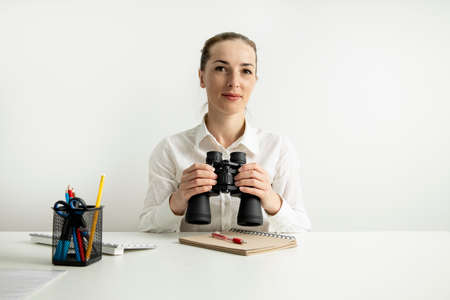 Young woman with binoculars sitting in the office at the workplace.の写真素材