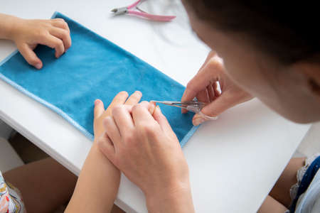 Mom does a manicure to her daughter cuts nails with nail scissors at homeの写真素材