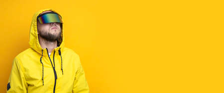 Young man in virtual reality glasses looks up on a yellow background. Banner.の写真素材