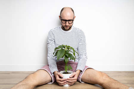 Young man sitting on the floor holding an indoor flower in a potの写真素材