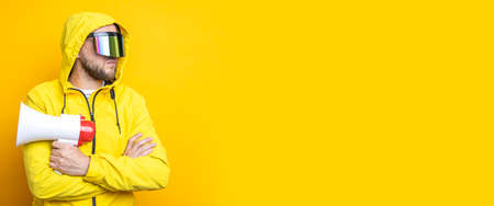 Young man in cyberpunk glasses holding a megaphone on a yellow background. Banner.の写真素材