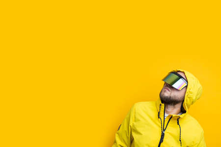 Young man in virtual reality glasses looking up on yellow background.の写真素材