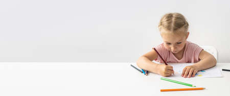 Blonde child girl draws with colored pencils sitting at the table. Banner.の写真素材