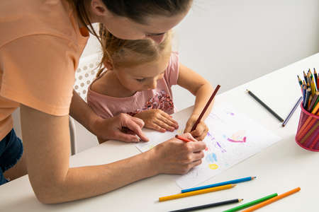 Mom and daughter draw together with colored pencils on paper at the table.の写真素材