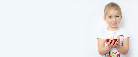 Smiling child girl blonde holding half an apple on a white background. Banner.の写真素材