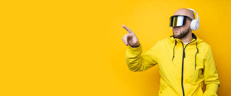 Young man in cyberpunk glasses with headphones clicking on an invisible screen on a yellow...