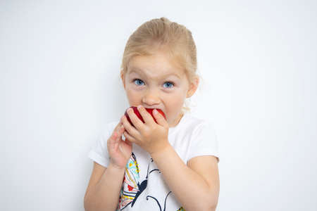 Child girl blonde eats an apple on a white background.