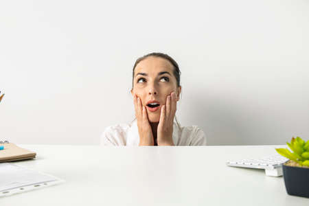 Surprised young woman looking up peeking out from under the desktop.の写真素材