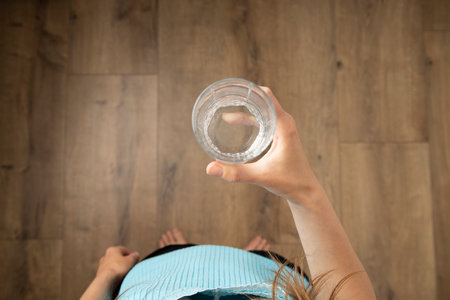Young woman holding a glass of water while standing on a wooden floor. Top view, flat lay.