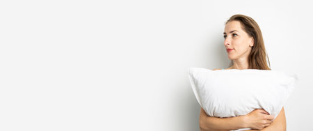 Smiling young woman in tank top holding pillow on white background. Banner.の写真素材