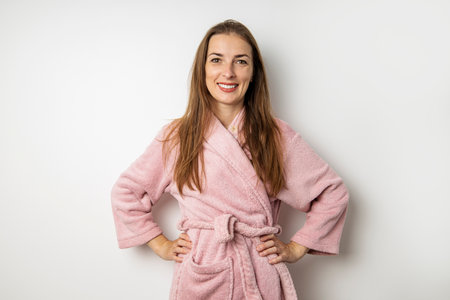 Smiling young woman in a pink bathrobe on a white background.の写真素材