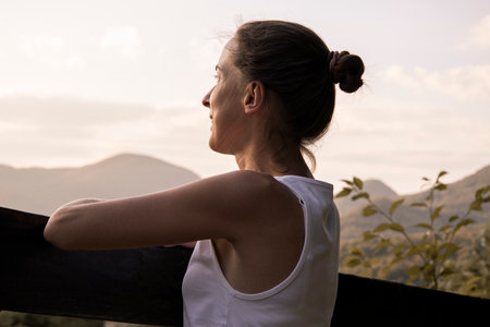 Young woman in a white tank top enjoys a beautiful natural landscape with mountain views.