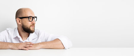 Young man holding hands folded while sitting at table on white background. Banner.の写真素材