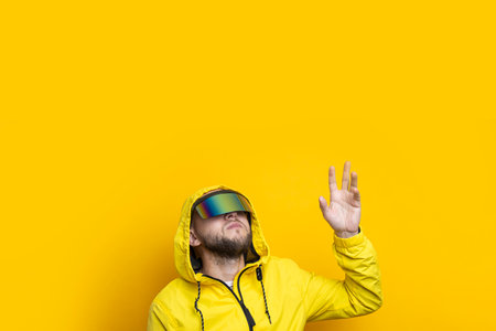 Young man in virtual reality glasses wants to take an invisible object on a yellow background.の写真素材