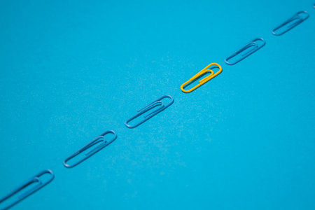 One yellow paper clip and blue paper clips on a blue background. Top view, flat lay.の写真素材
