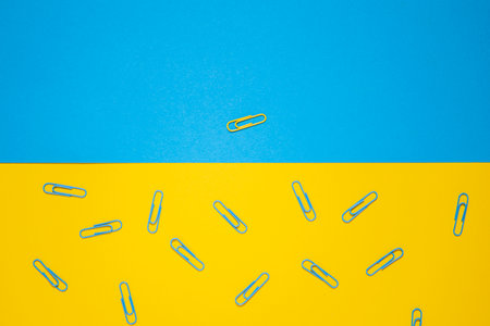 One yellow paper clip on a blue background, many blue ones on a yellow background. Top view, flat lay.の写真素材