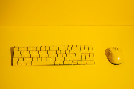Yellow wireless keyboard and yellow computer mouse on a yellow background.