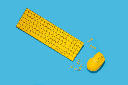 Yellow keyboard, wireless computer mouse, paper clips on a blue background. Top view, flat lay.の写真素材