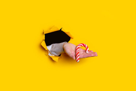 On a female palm holds a Christmas candy in a torn yellow background.の写真素材