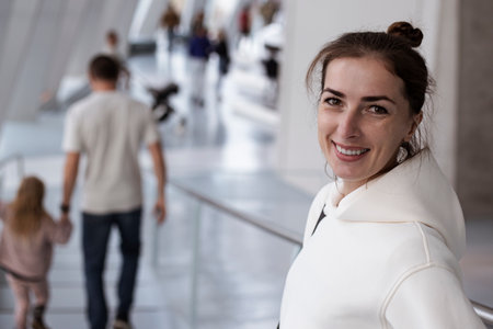 Smiling young woman in light hoodie standing indoors with bright light.