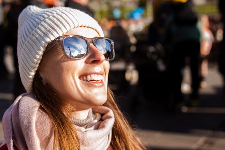 Smiling young woman in a hat with glasses on the street.の写真素材