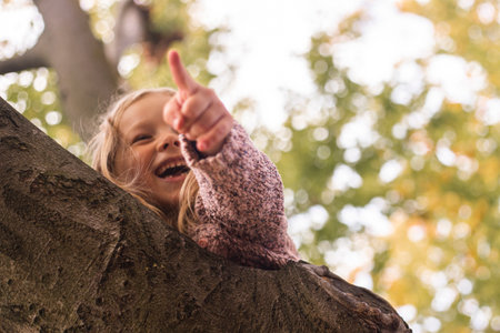 Smiling blond girl child points finger while lying on a tree.の写真素材