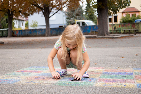 Child girl blonde preschool age is played on the pavement.