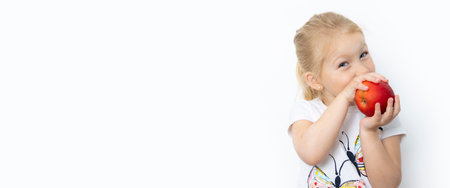Smiling child girl blonde holding an apple on a white background. Banner.の写真素材