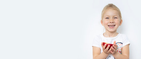 Smiling child girl blonde holding half an apple on a white background. Banner.の写真素材