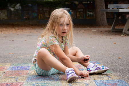 Child girl blonde preschool age is played sitting on the pavement.の写真素材