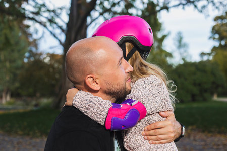 Joyful dad and little daughter in a helmet hugging in the park.の写真素材