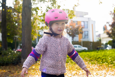 Smiling child girl in a helmet in protection roller blades in the park.の写真素材