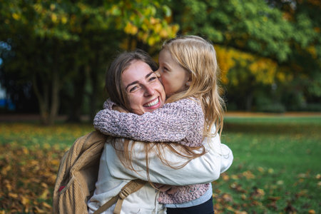 Young woman and child girl joyfully hugging in the park.