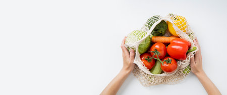 Women's hands hold a bag with fresh vegetables on a white table. Top view, flat lay. Banner.
