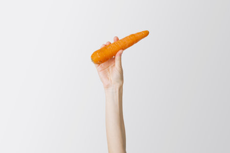 Woman's hand raised up a fresh carrot on a white background.の写真素材