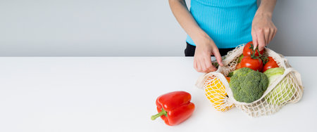 Women's hands take out fresh vegetables from a bag on a white table. Banner.の写真素材