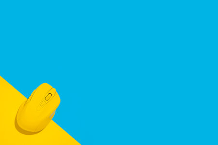 Yellow wireless computer mouse on a yellow blue background. Top view, flat lay.の写真素材