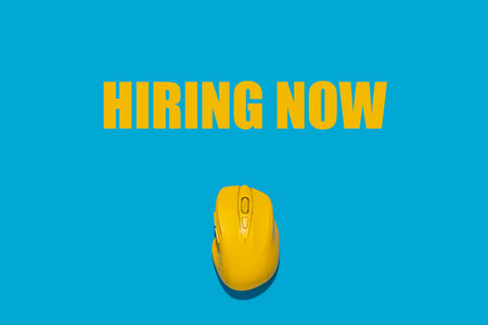 Yellow wireless mouse on a blue background, Hiring now added. Top view, flat lay.の写真素材