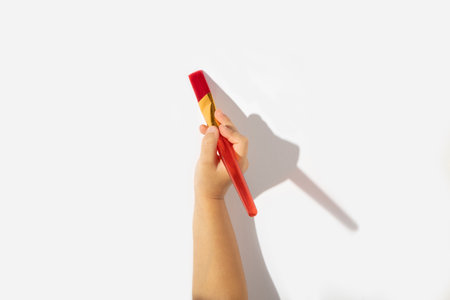 Child's hand holds a paintbrush on a white background. Top view, flat lay.の写真素材
