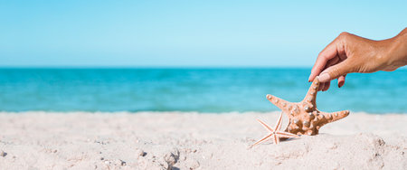 Female hand is touching starfish on a sandy beach. tropical nature. Banner.の写真素材