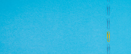 One yellow paper clip among blue paper clips on a blue background. Top view, flat lay. Banner.の写真素材
