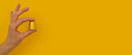 Woman's hand holding a coffee capsule on a yellow background. Banner.の写真素材