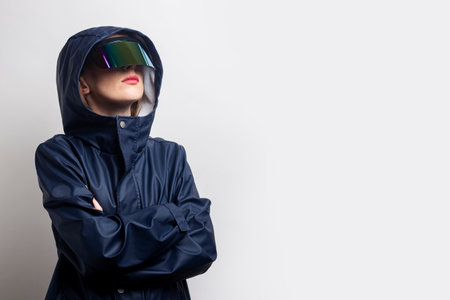 Young woman in virtual reality glasses, in a blue jacket with crossed arms on a light background.の写真素材