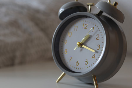 Retro alarm clock stands on a white bedside table near the bed.の写真素材