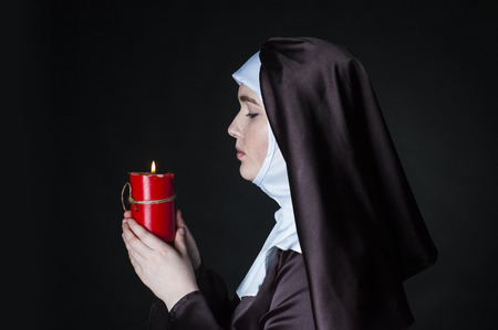 Young catholic nun is holding candle in her hands. Photo on black background. Side view.の写真素材