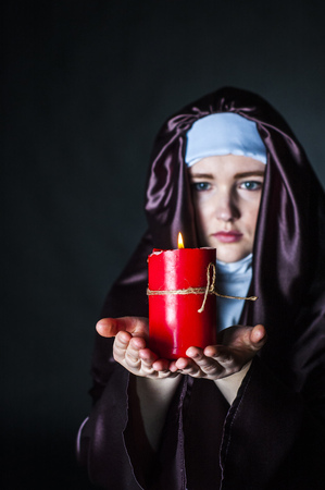 Young catholic nun is holding candle in her hands. Focus on candle. Photo on black background.の写真素材
