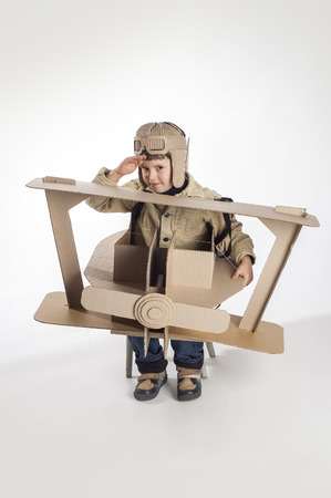 Boy in a pilots costume salutes. The action takes place near the cardboard airplane.の写真素材