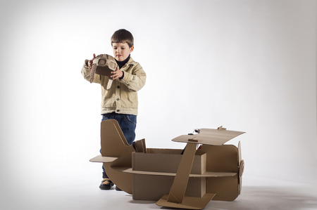 Young aviator in a homemade cardboard aircraft on gray background.の写真素材