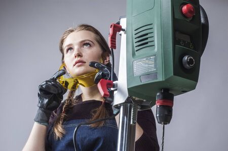 beautiful female carpenter at work using vertical drilling machine. close-up portrait.の写真素材