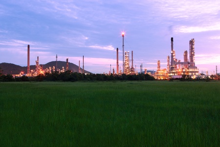 green grass field with scenic of petrochemical oil refinery plant shines at night 